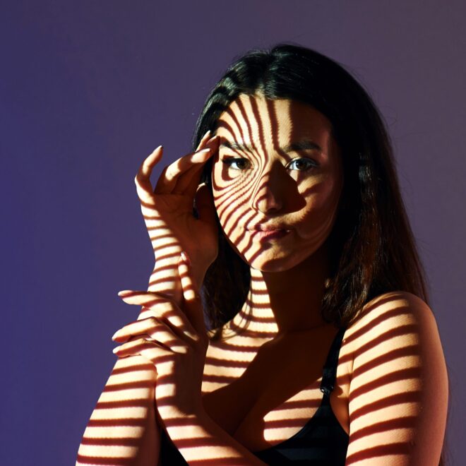 Eine Frau vor einem lila Hintergrund. Auf ihr Gesicht fällt ein leicht spiralförmiger Schatten