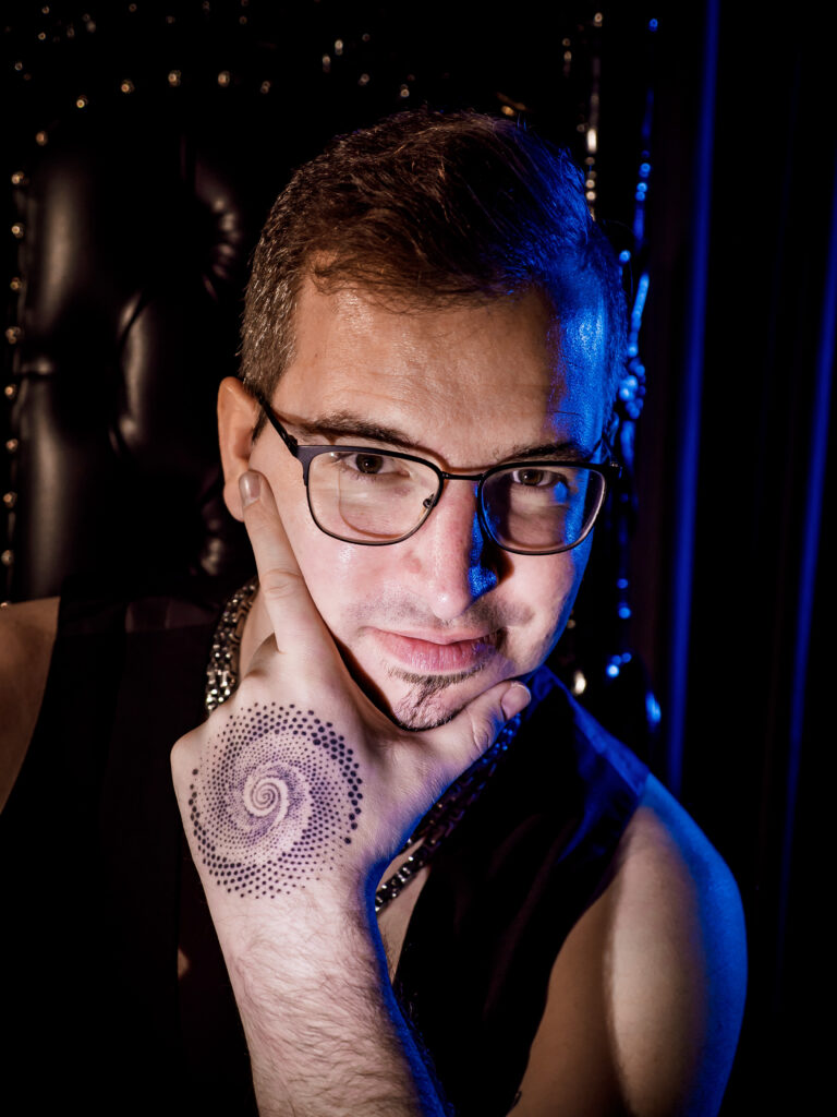 Eine Portrait Nahaufnahme von Mentor Chris mit Brille. ER stützt den Kopf mit seiner Hand auf deren Handrücken ein Spiraltattoo zu sehen ist