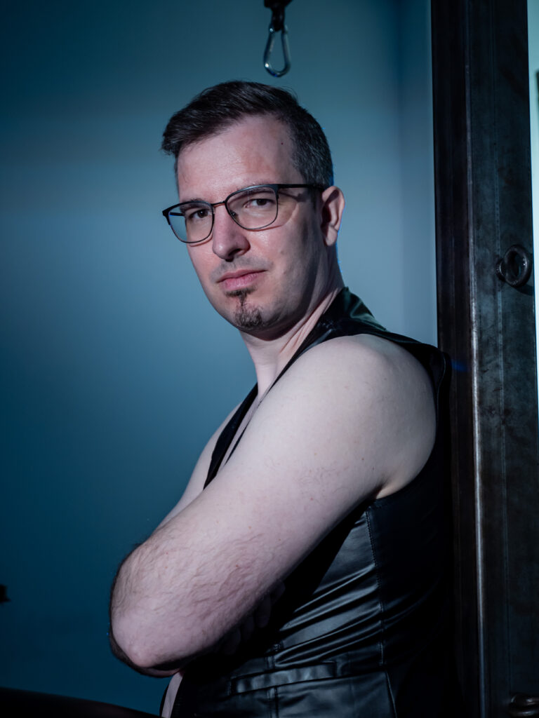 Mentor Chris lehnt mit dem Rücken an einem Stahlpfosten. Dabei trägt er eine Lederweste